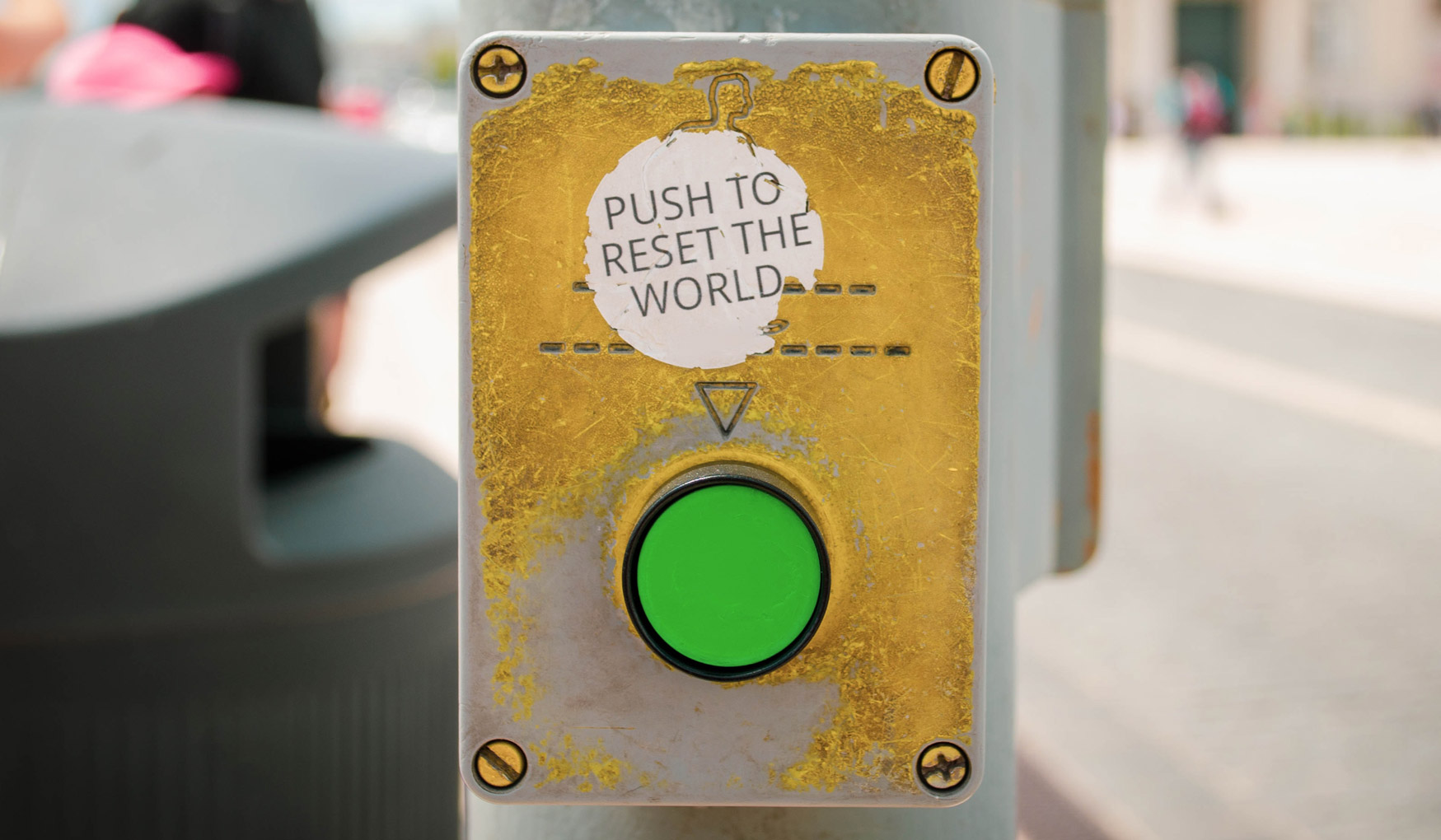 Crosswalk button affixed with a sticker saying, "push to reset the world".