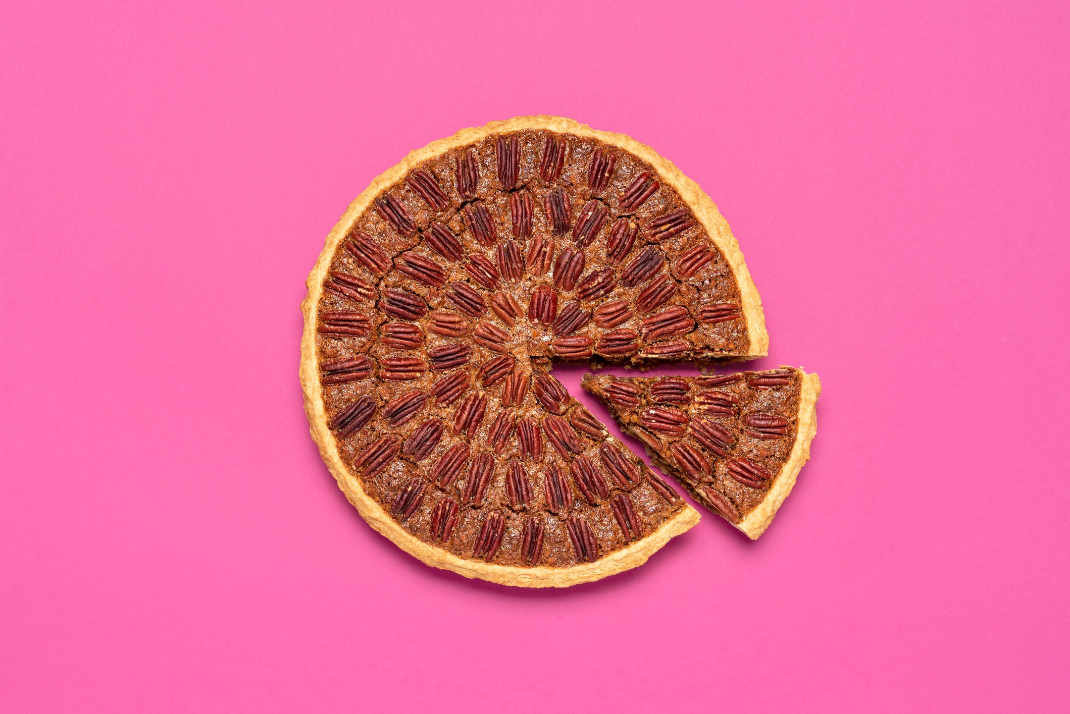 Pecan pie on pink background with a slice pulled out.